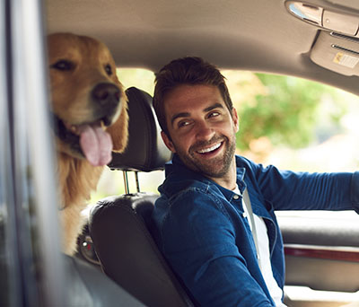 A man sitting in his car and smiling at his dog in the back seat.
